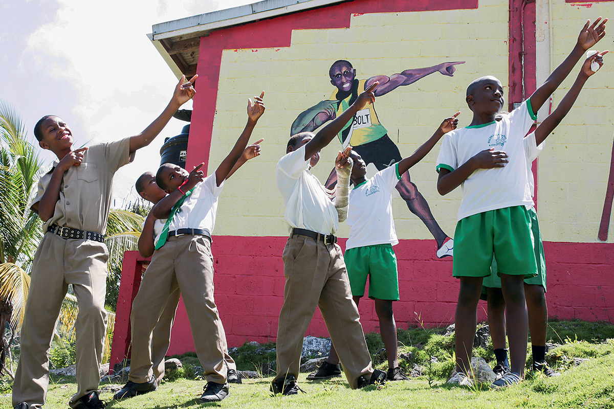 As crianças fazem o clássico gesto de Bolt em frente à escola onde ele estudou